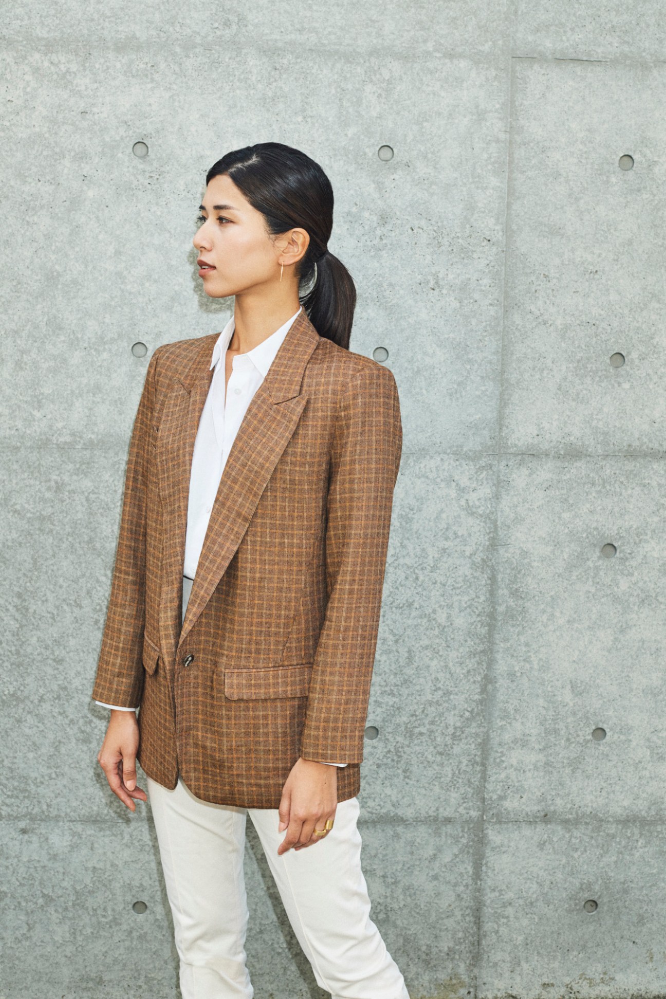 Woman wearing a tan checkered blazer and white shirt against a concrete wall.