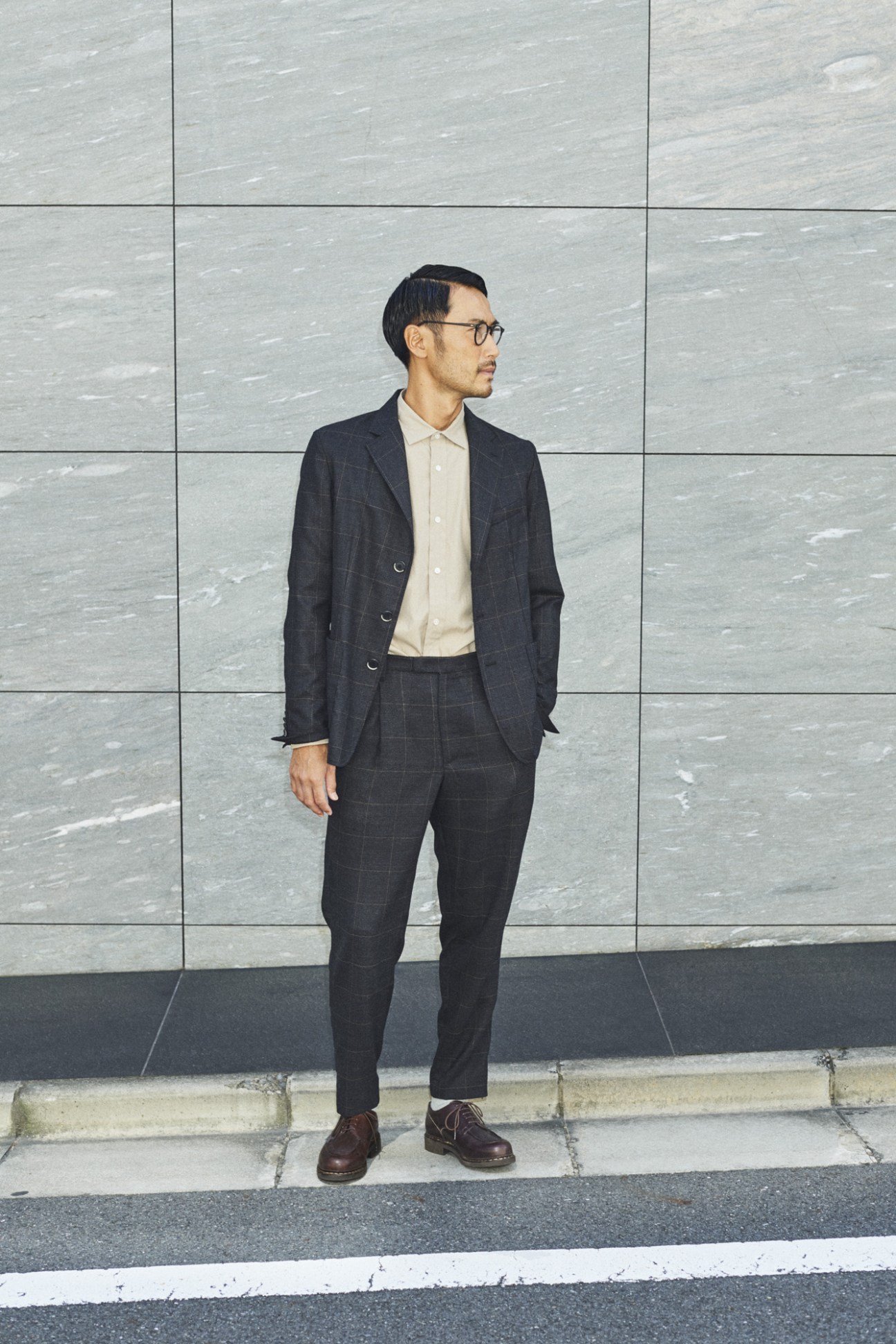 Man wearing Barena Venezia jacket and trousers with Auralee shirt, standing against grey tiled wall.