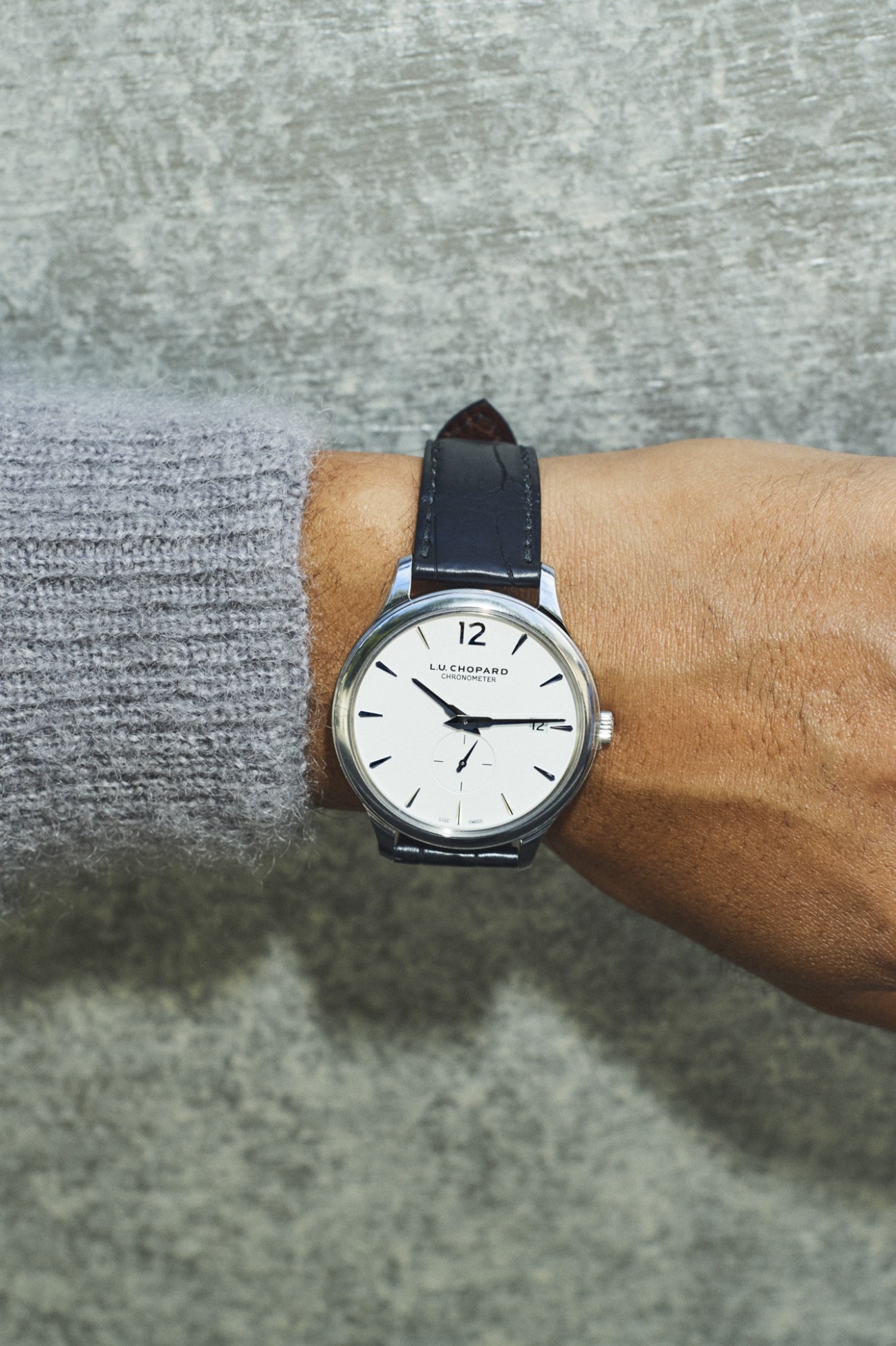 Wrist-worn luxury watch with silver case, white dial and black leather strap.