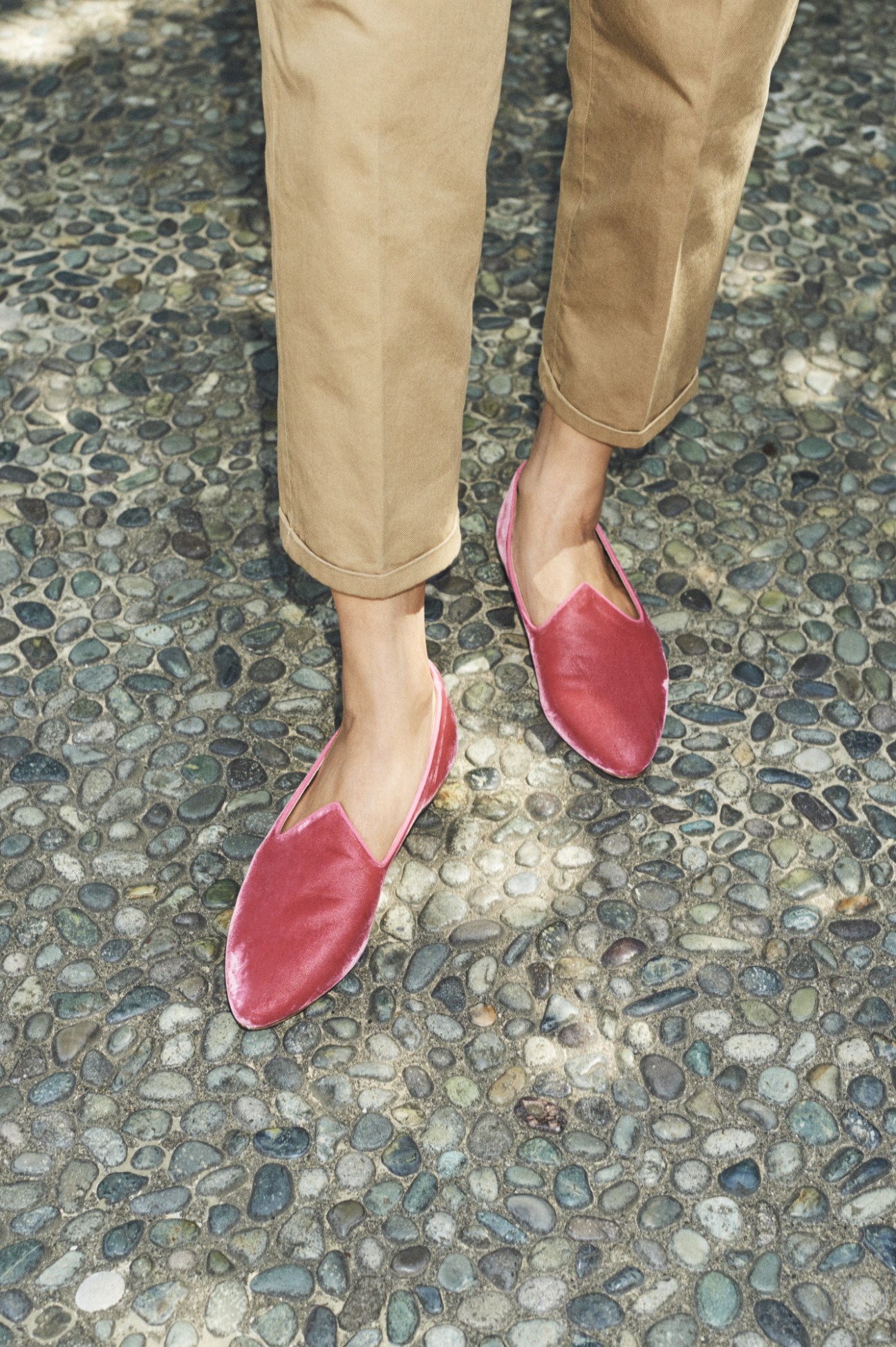 Woman wearing beige cropped trousers and red velvet slip-on shoes standing on cobblestone pavement.
