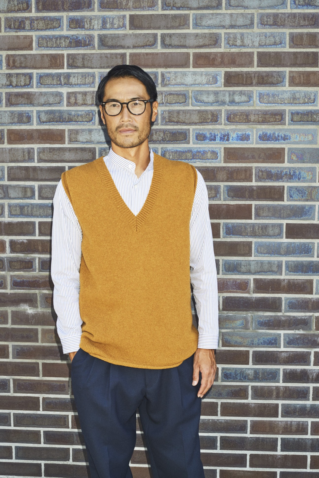 Man wearing Ermenegildo Zegna blazer and accessories standing against brick wall