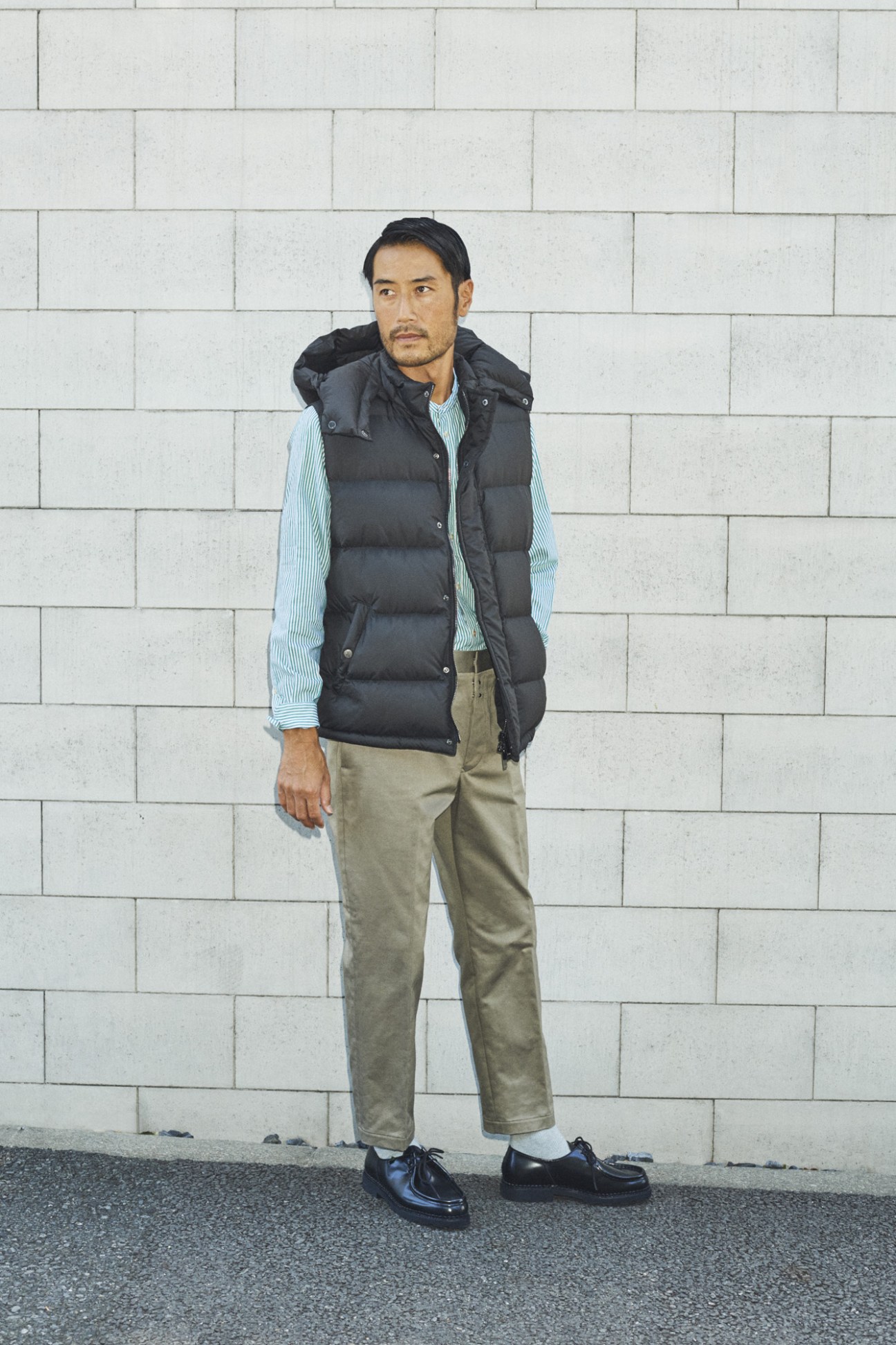 Man wearing a chunky textural McConnell Woollen Mills jumper and Barena Venezia trousers against a white brick wall.