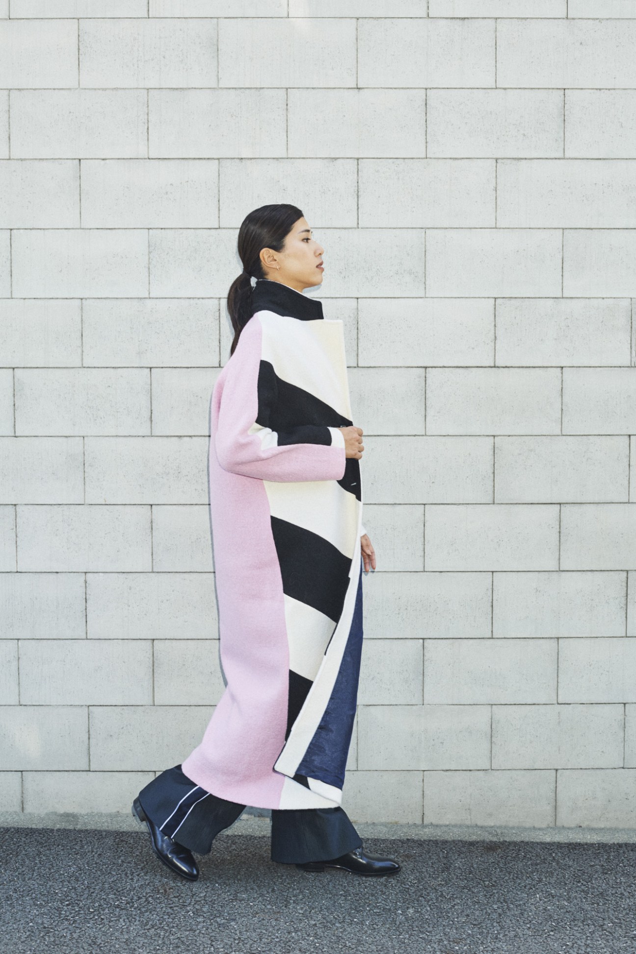 Woman wearing a pink and black color-block knit wrap against a white tile wall.