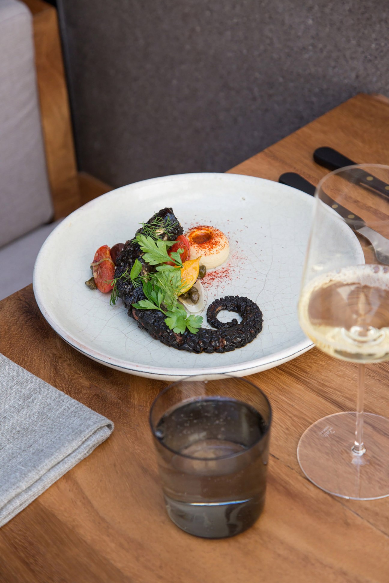 Plated octopus dish at Pujol restaurant with garnish and wine glass on wooden table.