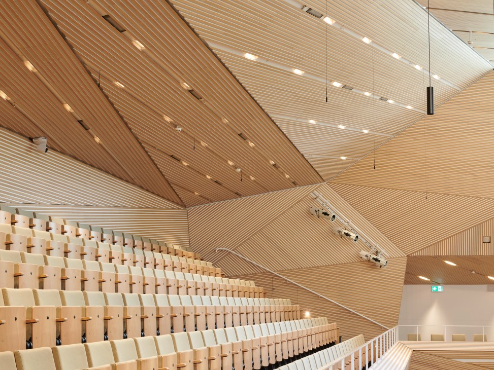 Interior view of Andermatt Concert Hall showing wooden ceiling with linear slats and integrated lighting.