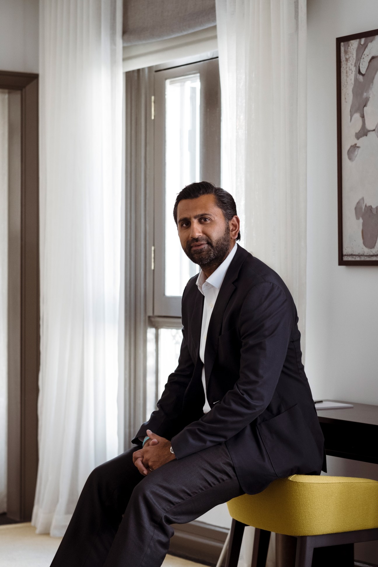 Ashish Manchharam, founder of 8M real estate company, sitting in a modern interior space with white curtains and minimalist decor.