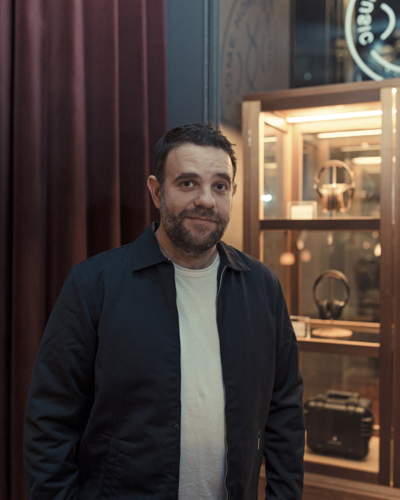 Paul Noble, co-founder of Spiritland, stands in front of a display cabinet containing audio equipment and headphones.