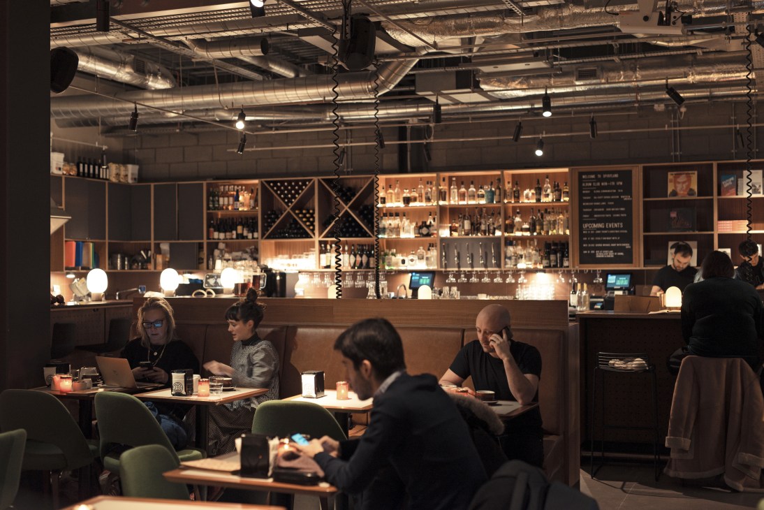Interior view of Spiritland bar and restaurant with wood-panelled seating, illuminated shelving displaying bottles, and patrons at tables.