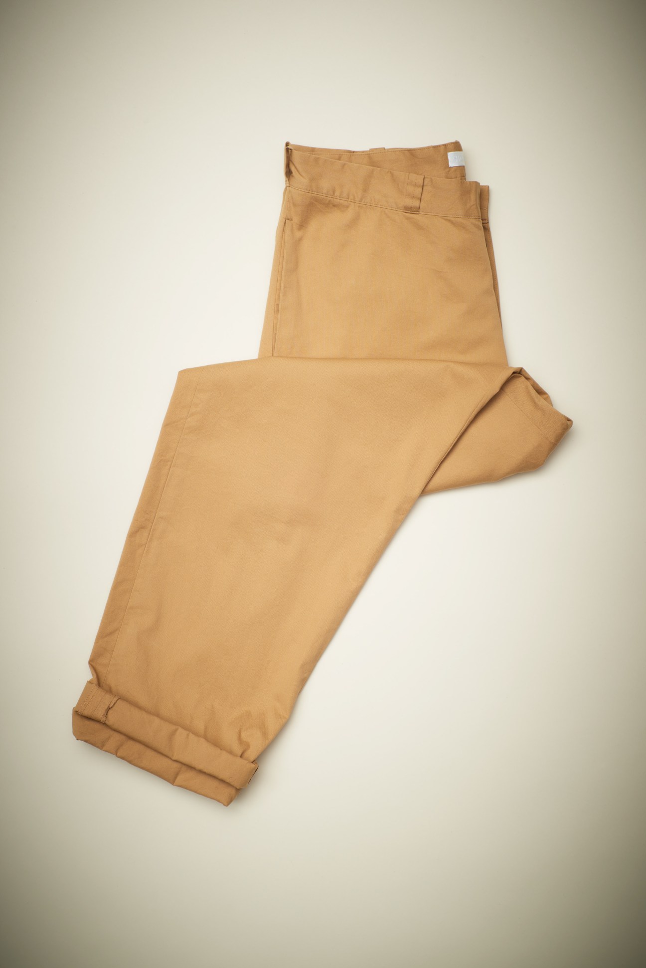 Tan cotton trousers with cuffed ankles and a white label visible at the waistband.