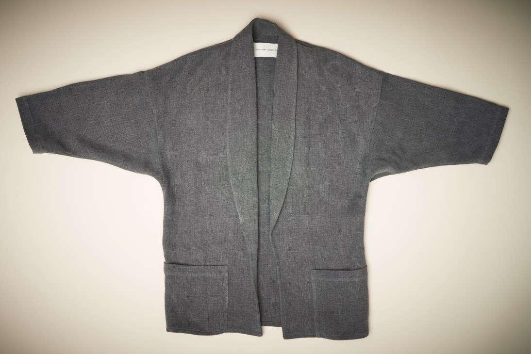 Gray linen coat laid flat against a neutral background displaying its pared-back design.