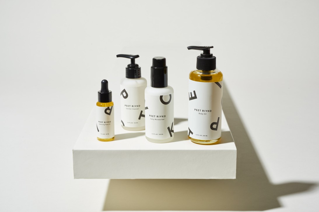 Peet Rivko skincare products displayed on white platform including cleanser, moisturizer and body oil.