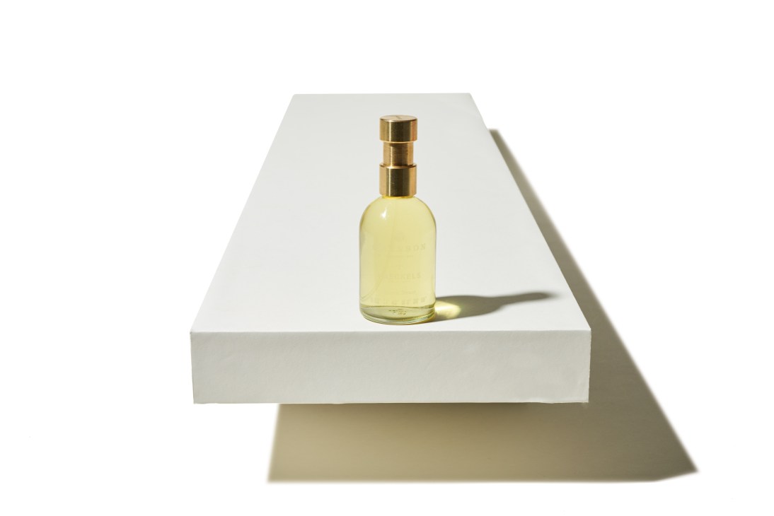 Pale yellow fragrance bottle with gold atomizer on white surface casting shadow.