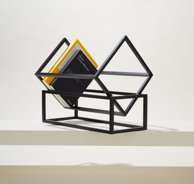 Black steel geometric magazine rack by Kristina Dam Studio with triangular and rectangular frames holding books.