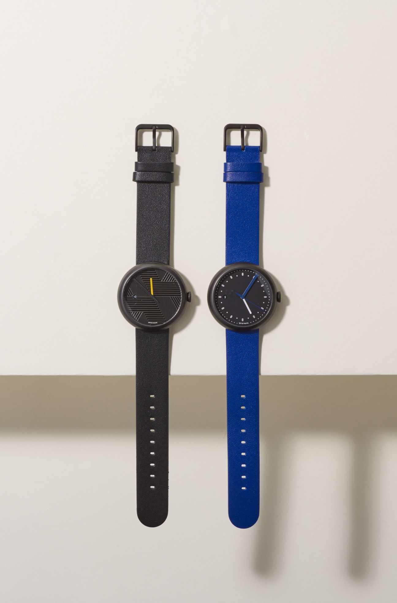 Two Objest watches with geometric dial patterns on black and blue leather straps.