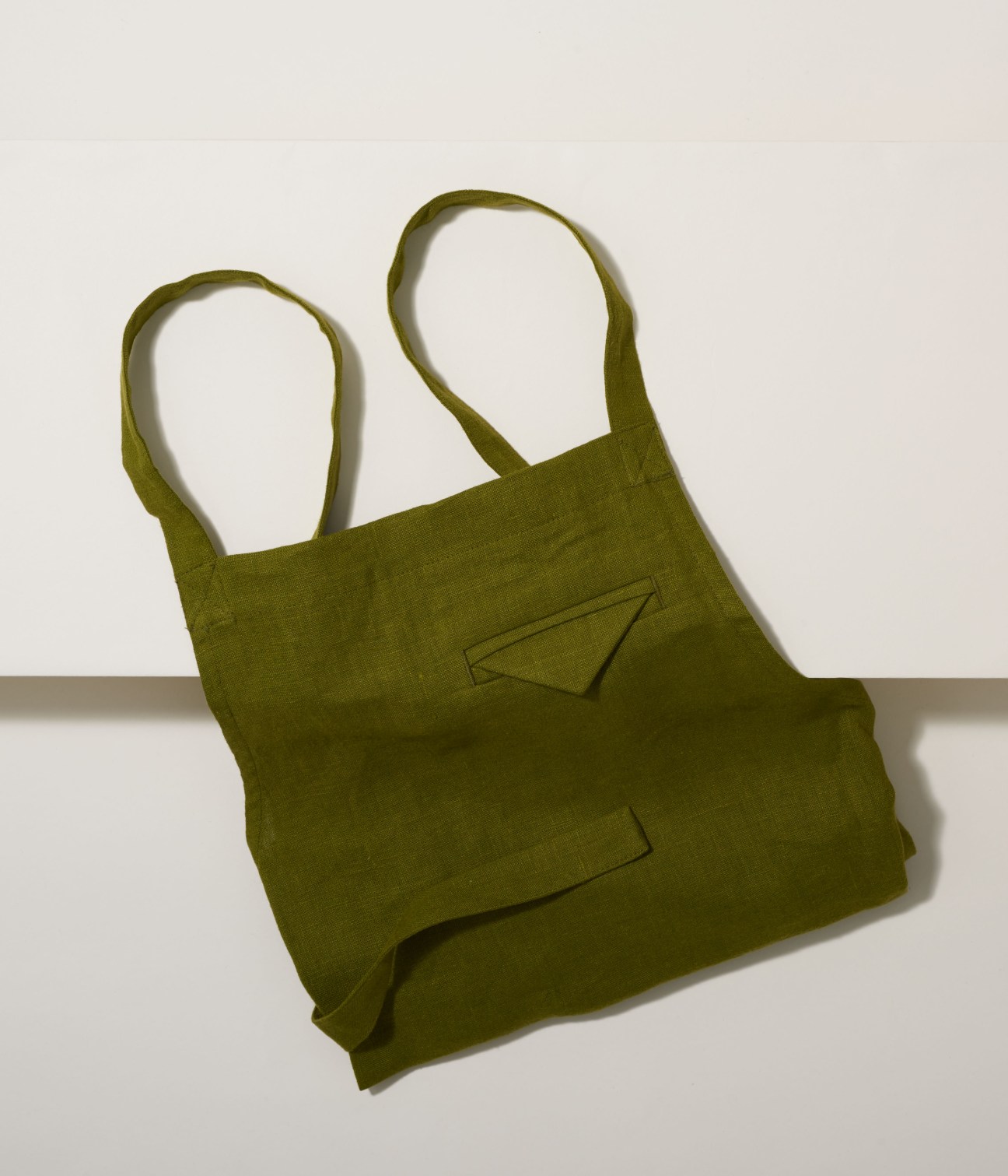 Olive-green linen apron with embroidered pocket details and long shoulder straps.