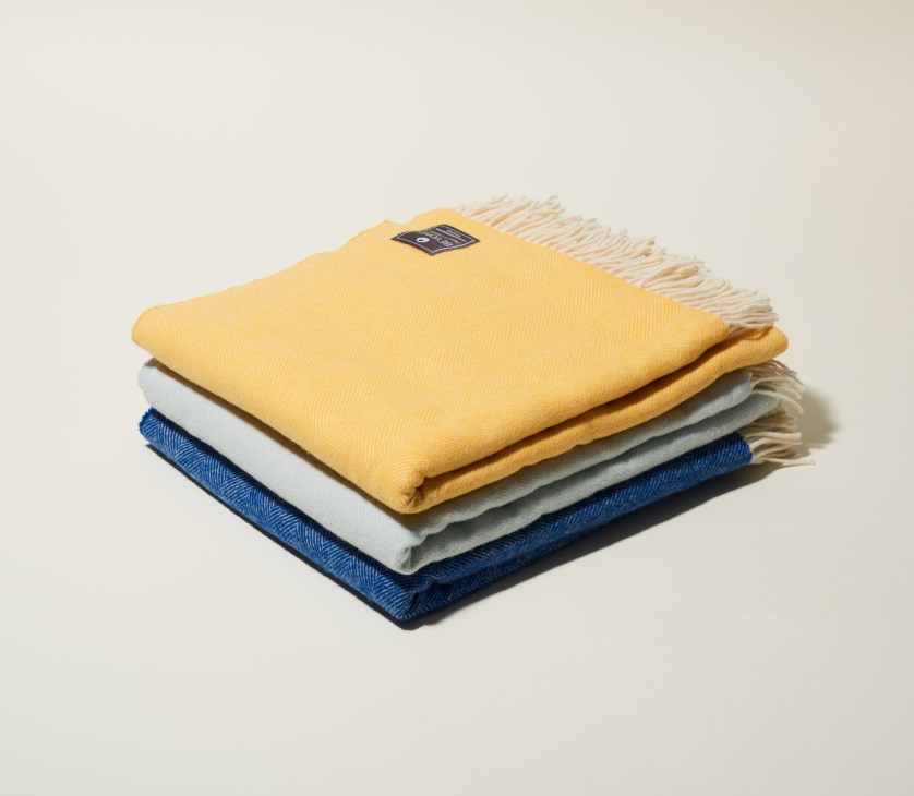 Stacked merino wool throws in yellow, white, grey and navy blue with fringed edges.