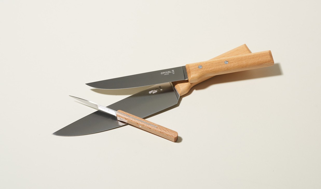 Three Opinel kitchen knives with wooden handles arranged on a neutral background.
