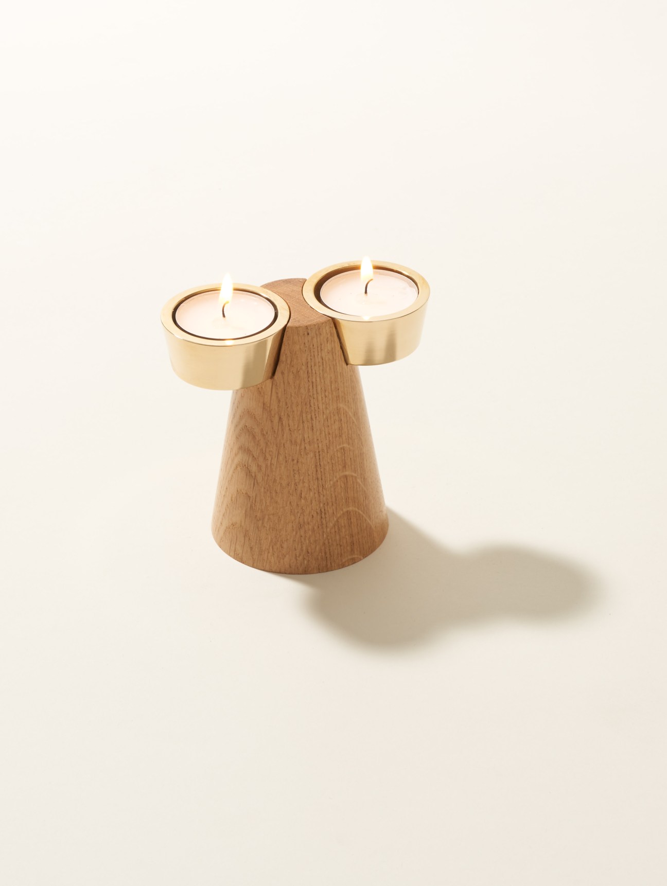 Wooden candleholder with two brass cups holding lit candles by Caussa designer Andreas Kowalewski.