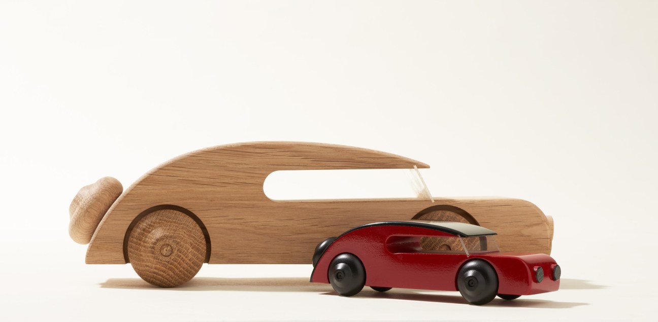 Wooden toy cars in streamlined 1930s sedan style, one natural oak and one painted red.