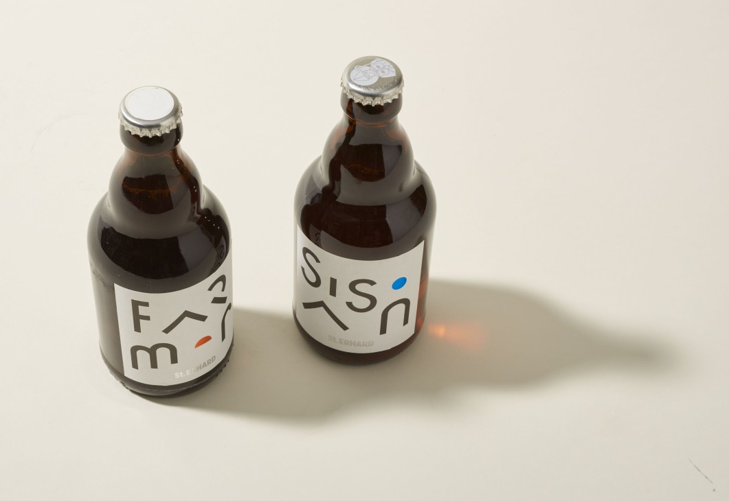 Two brown glass St Erhard beer bottles with minimalist geometric label designs on cream background.
