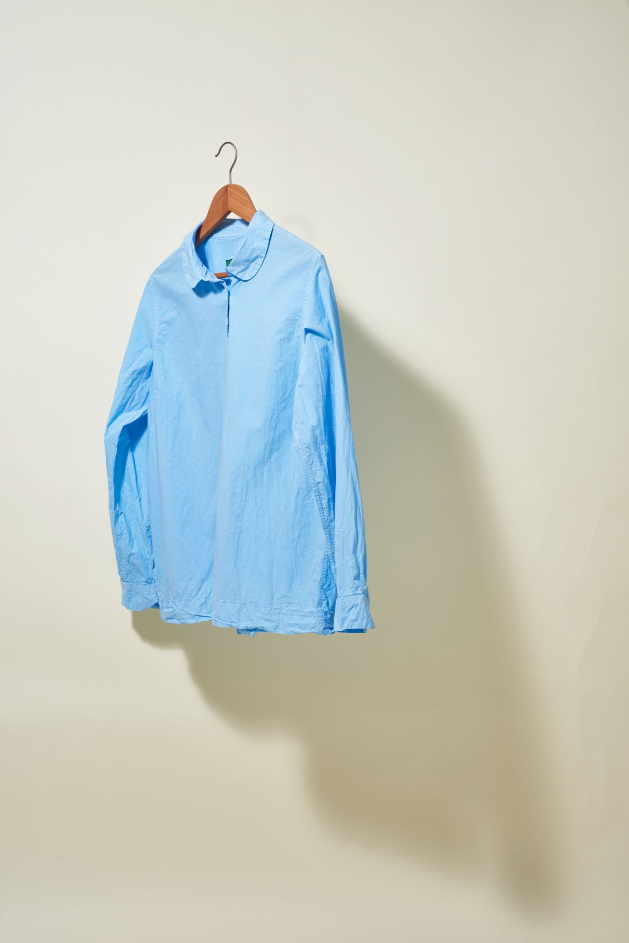 Light blue button-up shirt on wooden hanger against neutral background.