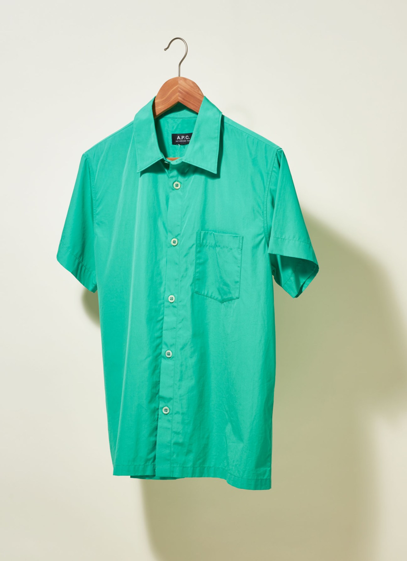 A.P.C. short-sleeved turquoise button-up shirt on a wooden hanger against a neutral background.