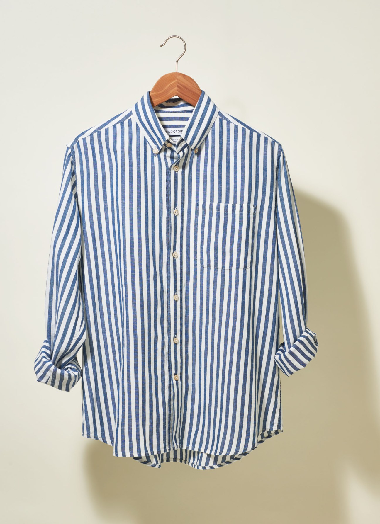 Blue and white striped button-down shirt on wooden hanger against neutral background.