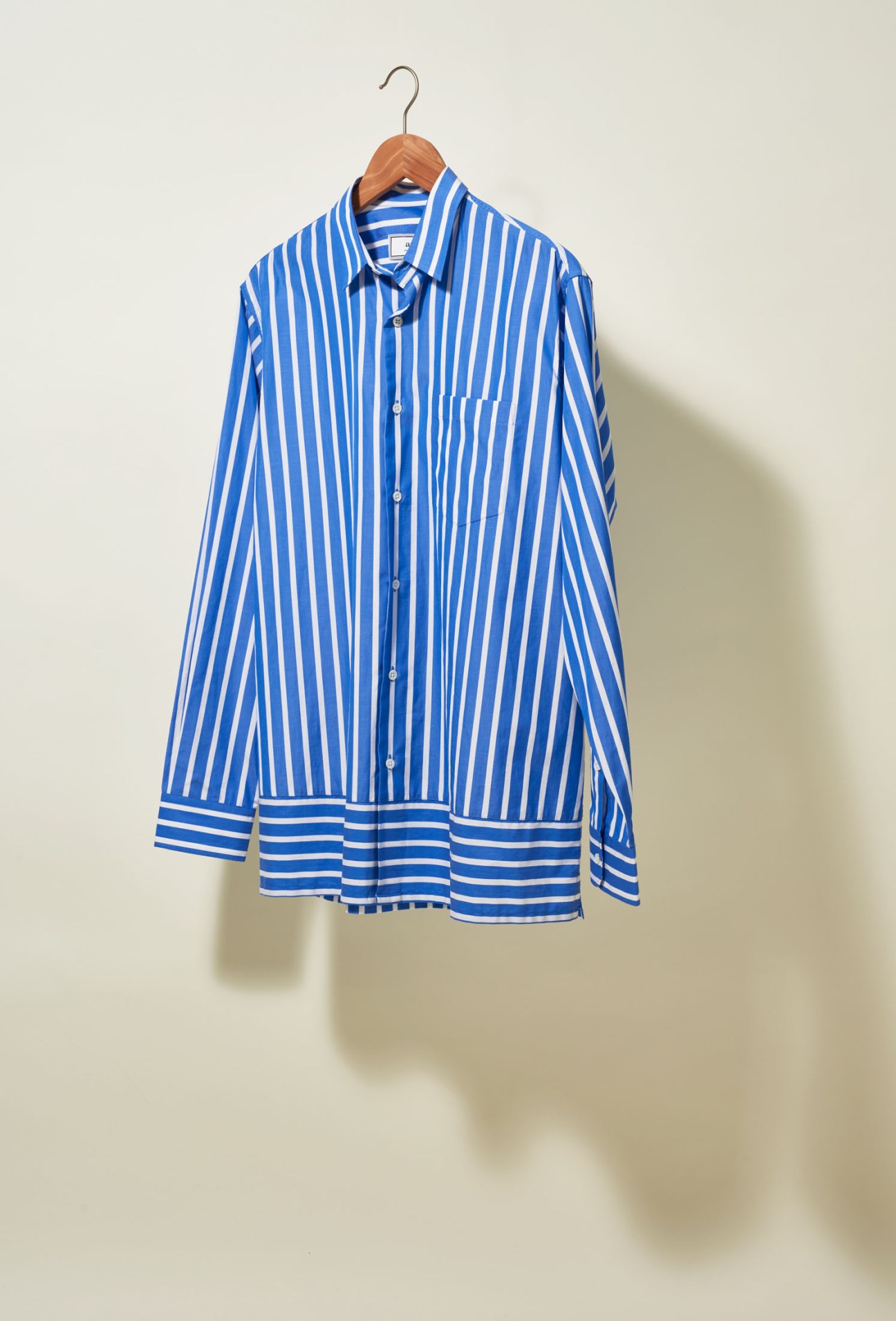 Blue and white striped poplin shirt by Ami displayed on a wooden hanger against a neutral background.