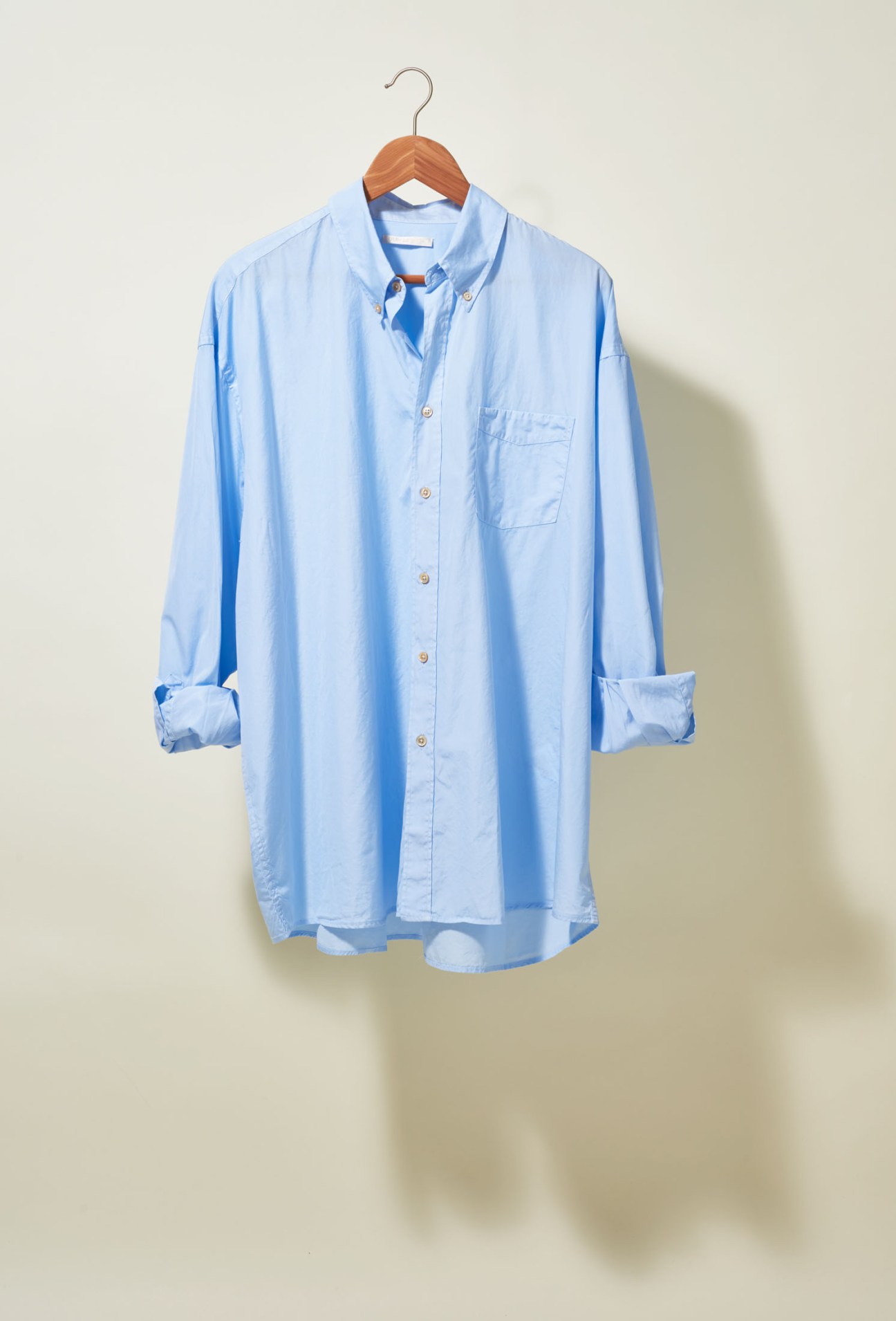 Light blue button-down shirt with rolled sleeves on a wooden hanger against a neutral background.