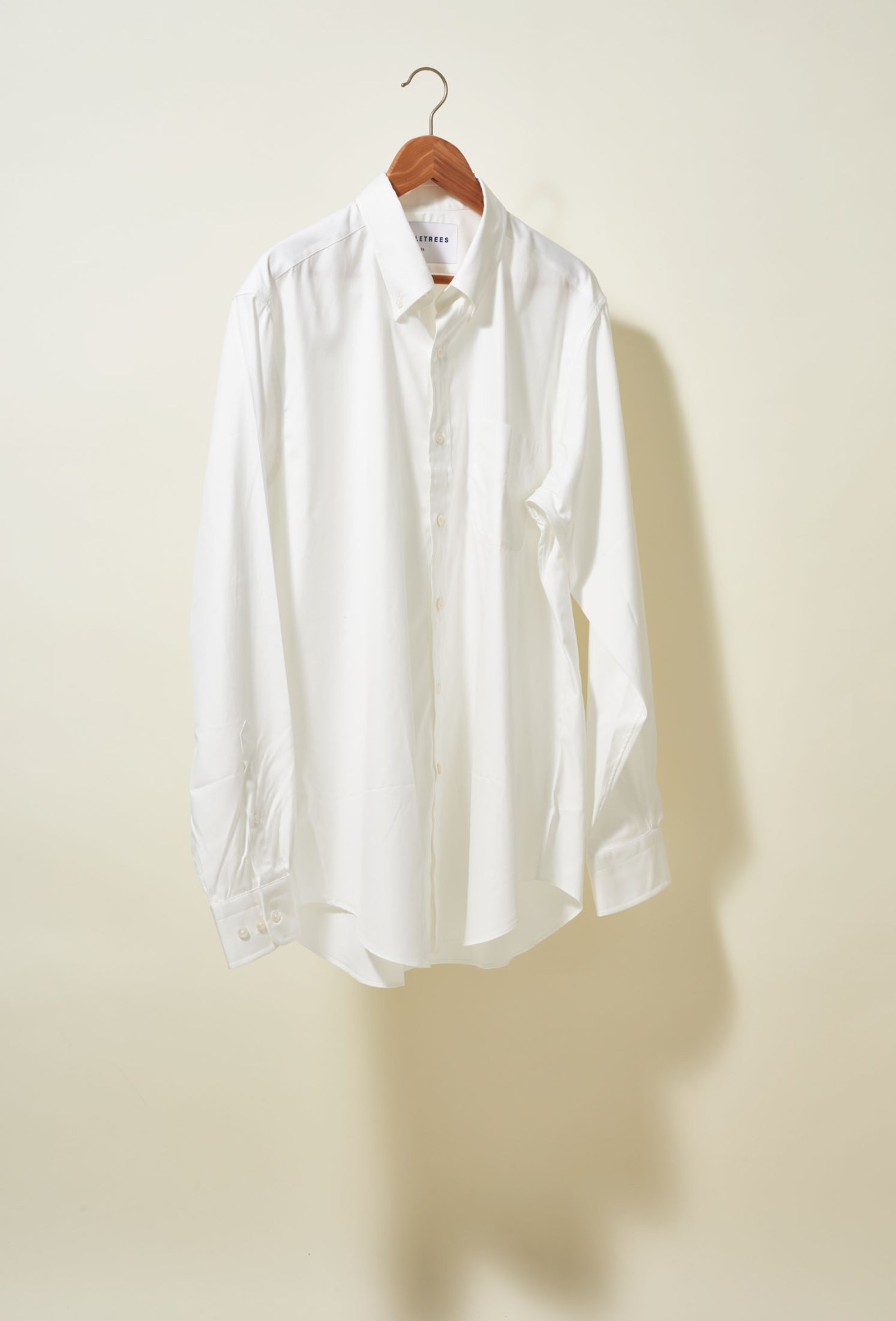 White cotton button-down shirt on wooden hanger against neutral background.