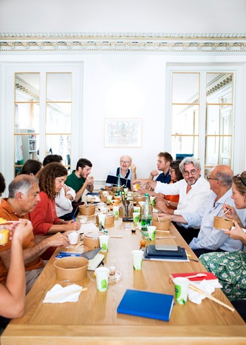 Team members at Le 1 newspaper gather around a dining table for their weekly Monday lunch meeting in Paris.