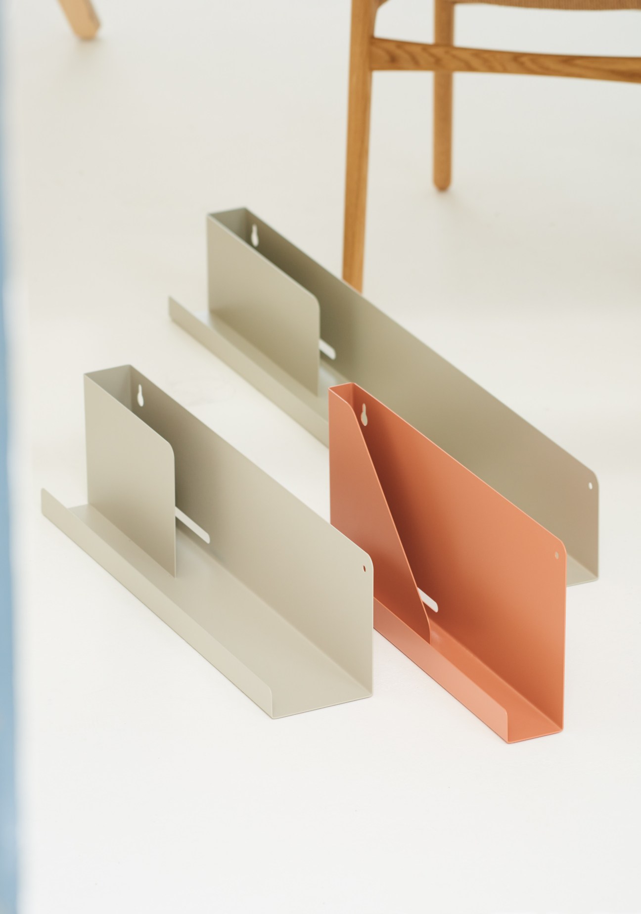 Three folded metal shelf units in cream and terracotta, demonstrating curved pocket storage design.