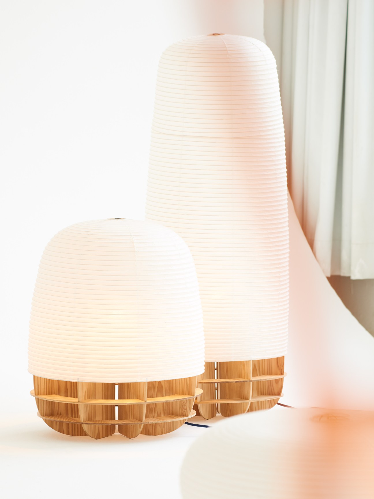 Two illuminated white paper lanterns with wooden base frames against a white background.