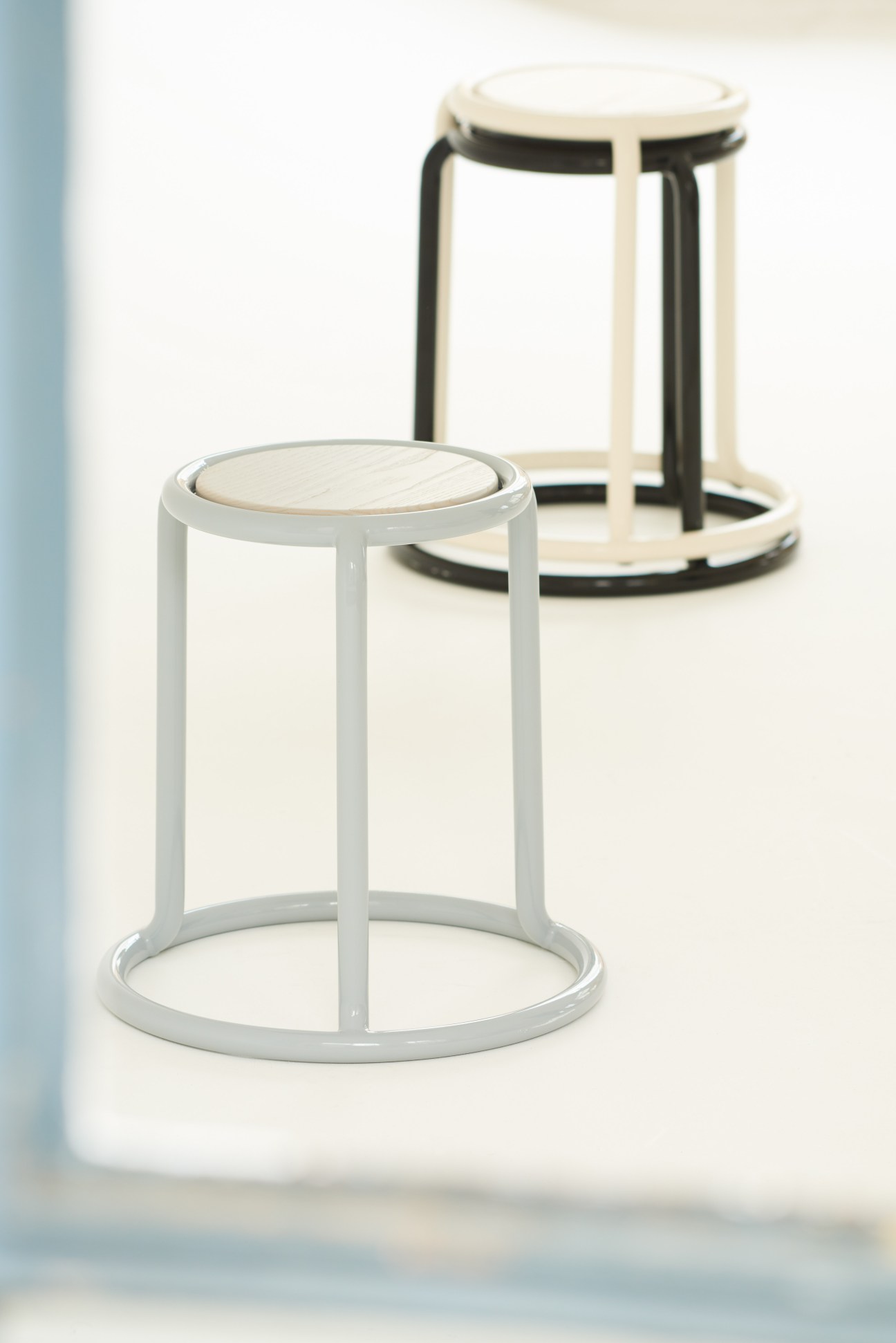 Two stackable stools with tubular steel frames and round wooden seats in white and black finishes.