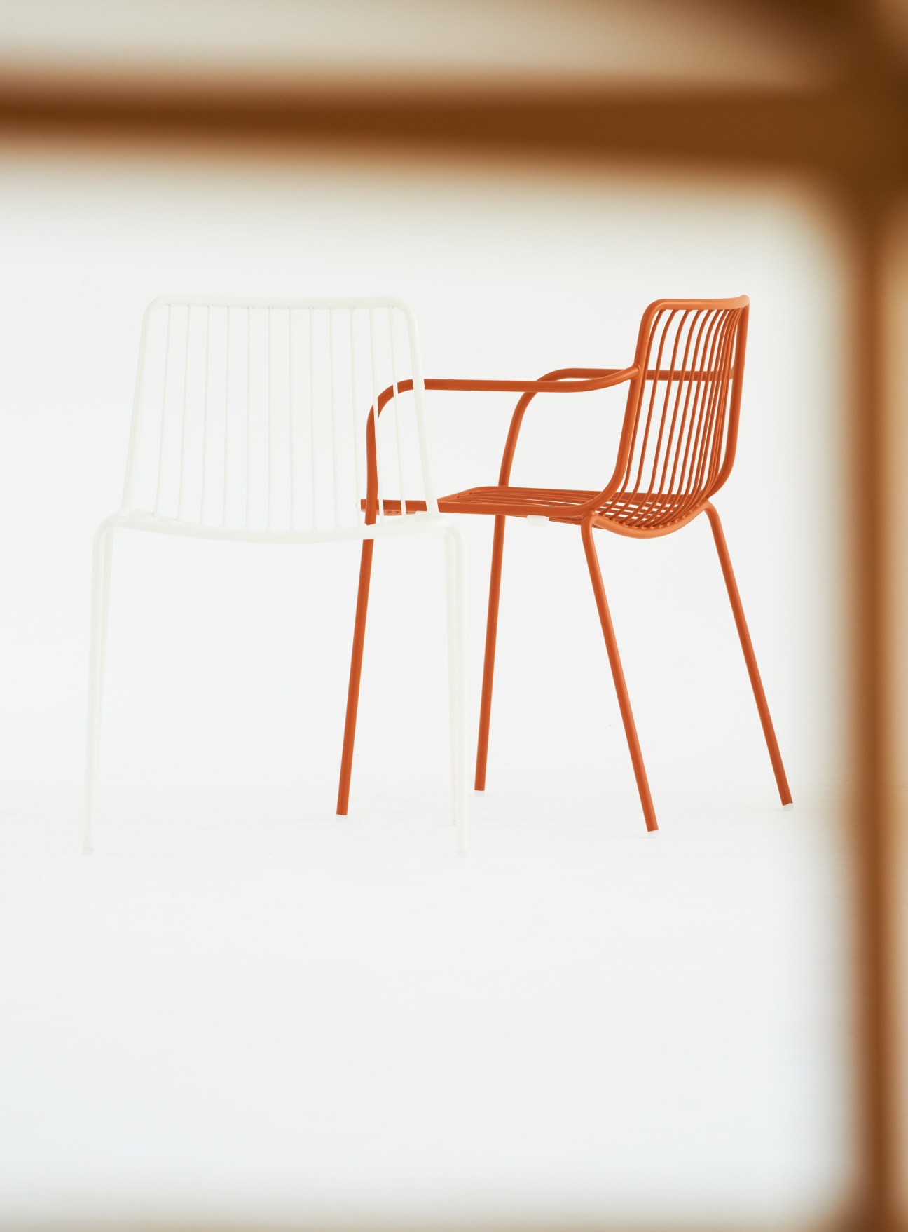 Orange and white metal chairs with vertical slat backs and armrests against a neutral background.