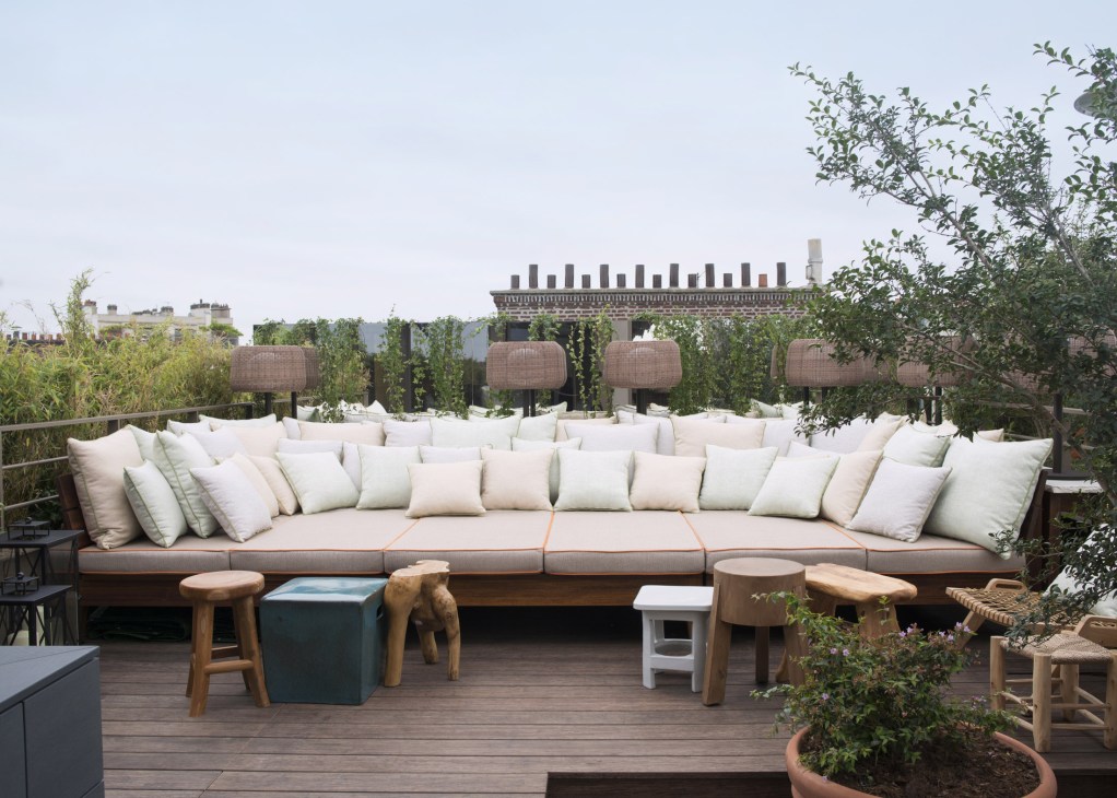 Brach hotel rooftop terrace with long cushioned seating, wooden stools, and Parisian skyline views.
