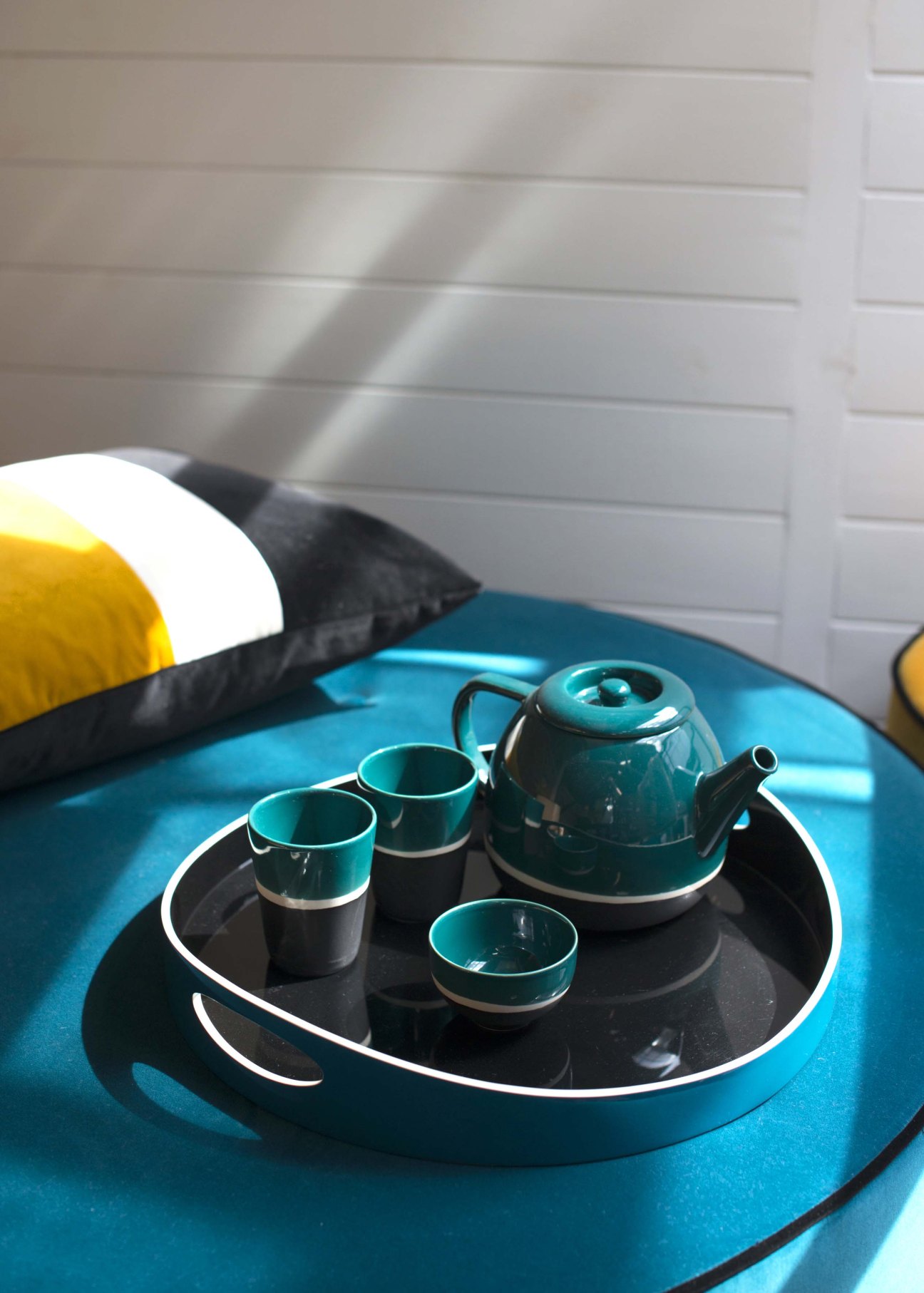 Turquoise tea set with teapot and cups on black tray displayed on blue surface