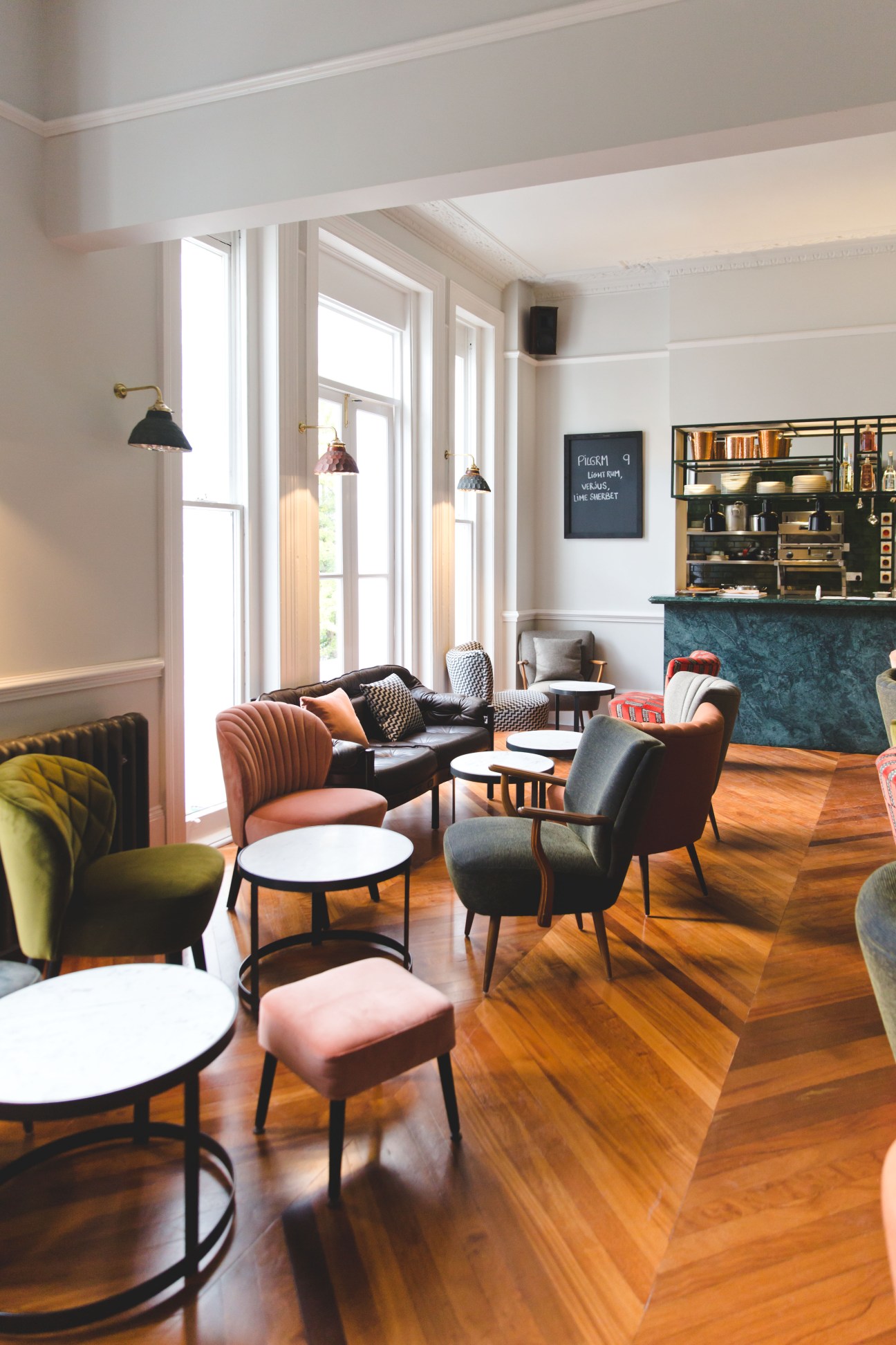 Interior of The Pilgrm hotel lounge with colorful mid-century chairs, small tables, and a bar area in London.
