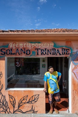 Man standing in doorway of orange shop with Solano Trindade signage in Campo Limpo, São Paulo.