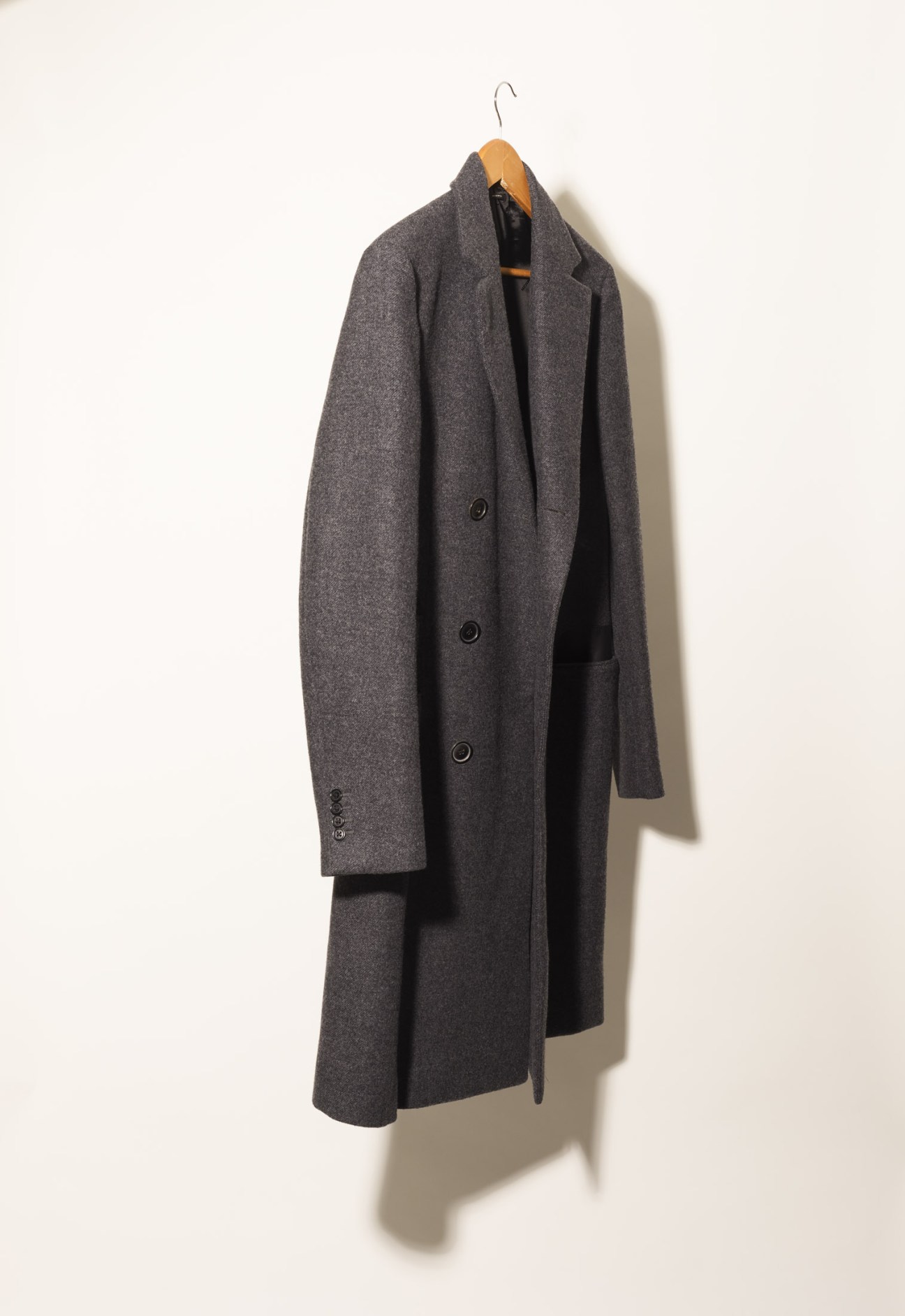Hermès double-breasted taupe coat hanging on wooden hanger against white wall