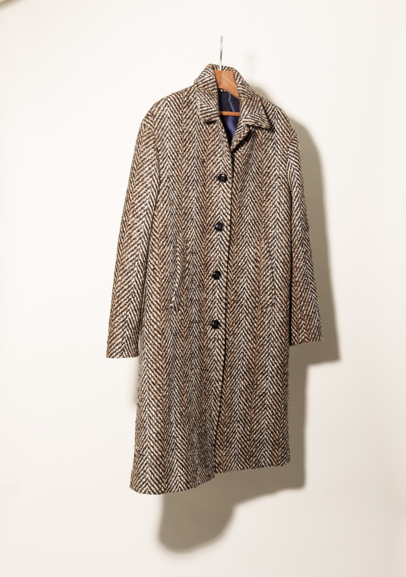 Drumohr herringbone wool overcoat in neutral tone hanging on wooden hanger