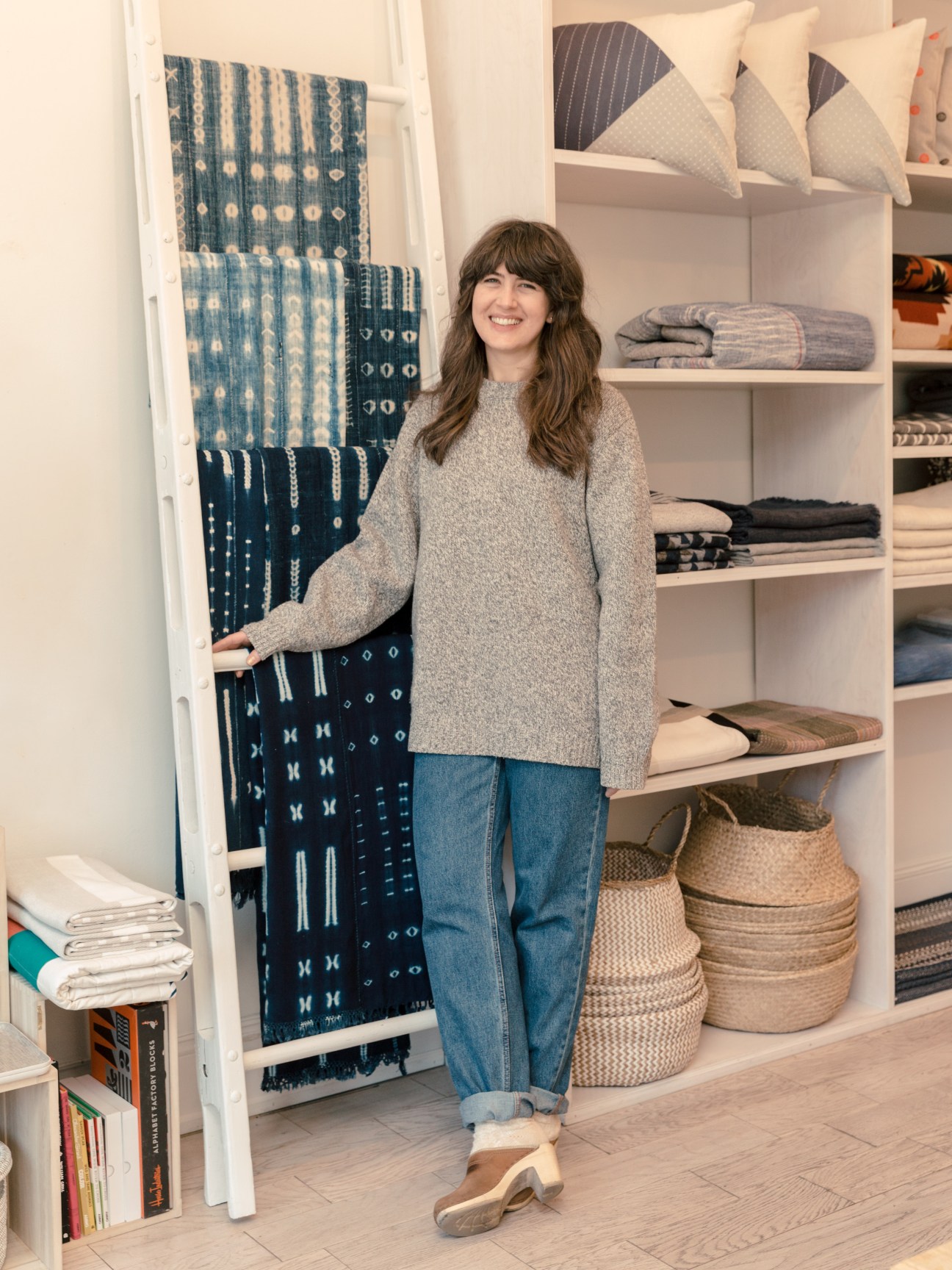 Woman smiling while displaying blue patterned textiles and home goods on white shelving unit.