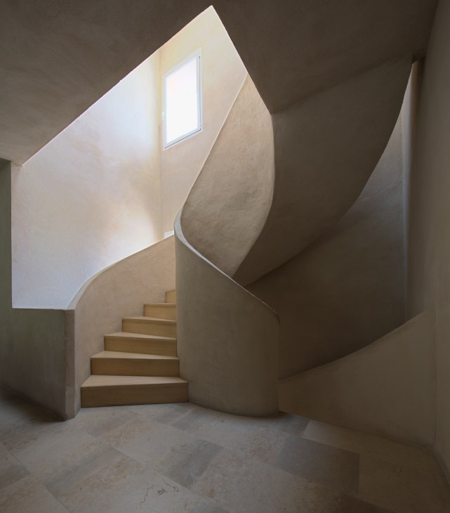 Sinuous sweeping staircase with curved concrete walls and pine treads lit by upper window in Fernando Caruncho's Madrid studio.