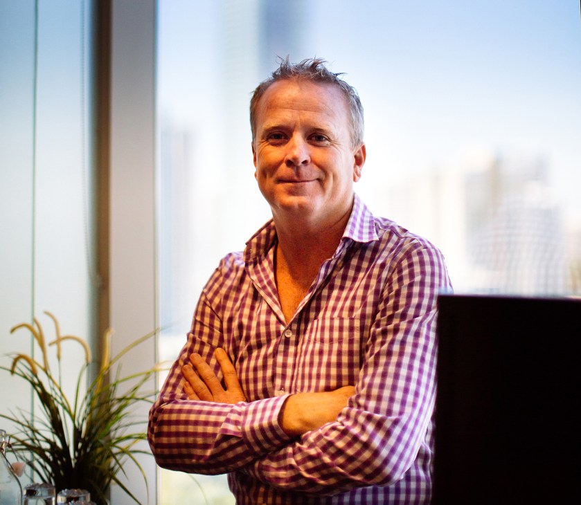 Danny Maher, founder of Opmantek, poses for a portrait in a high-rise office with city views behind him.