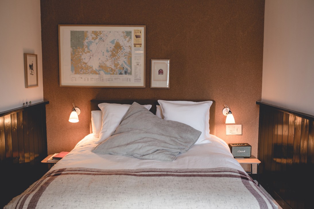 Minimalist hotel bedroom with natural materials, cork walls, and framed artwork above the bed at Le Barn.