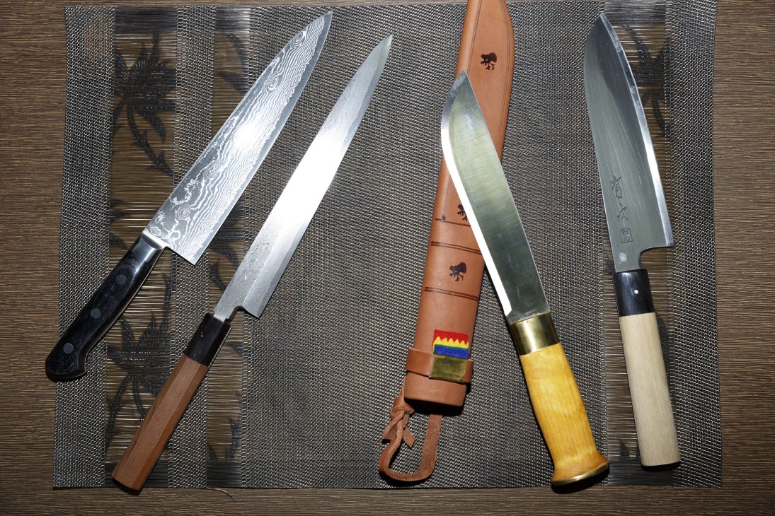 Collection of kitchen knives with various blade styles and handle materials arranged on a textured surface.