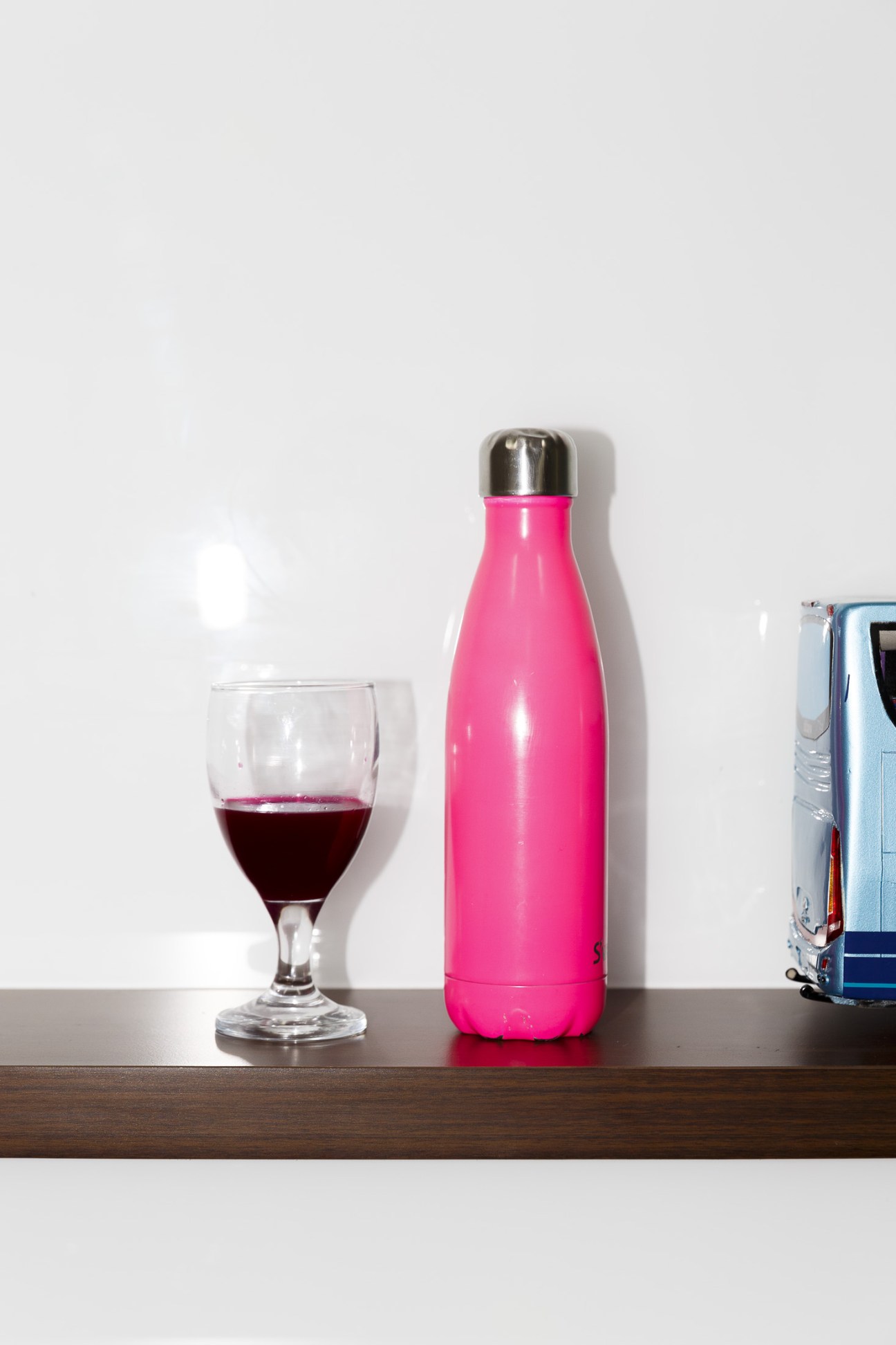 Pink water bottle next to a glass of dark red detox juice on a wooden surface.
