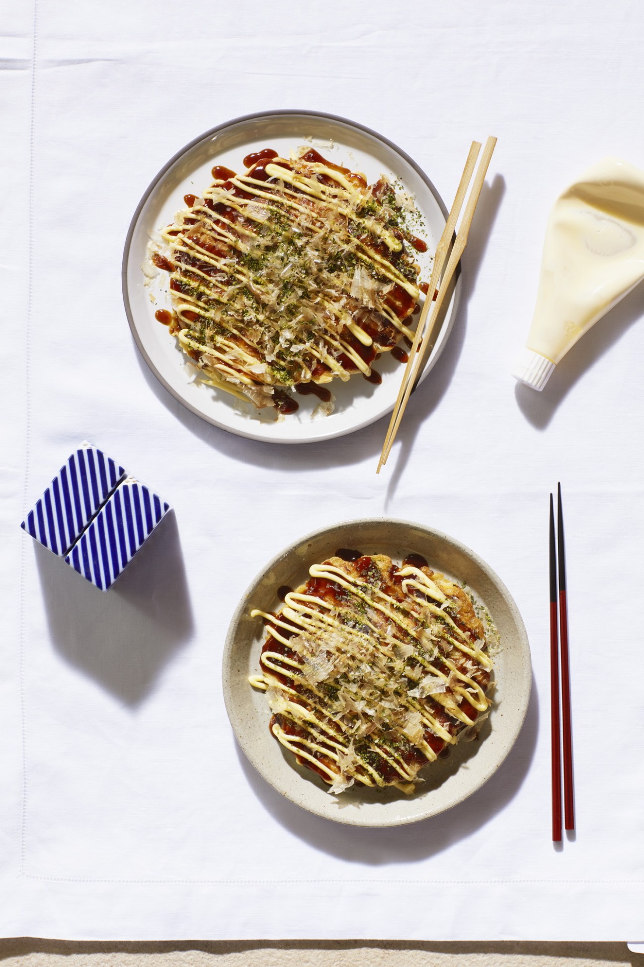 Okonomiyaki pancakes garnished with mayonnaise, bonito flakes and seaweed powder on white plates