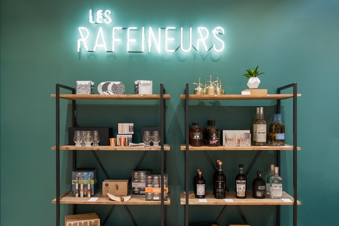 Les Raffineurs Paris pop-up shop display with neon sign, wooden shelves, bottles, glasses and home accessories.