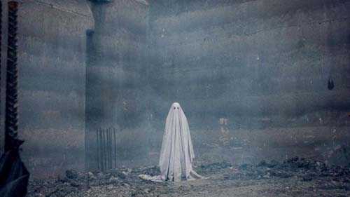 A figure in a white sheet standing in a desolate, dusty landscape from the film A Ghost Story.